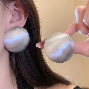 Detail of oversized round silver studs showing brushed texture and cat-eye luster