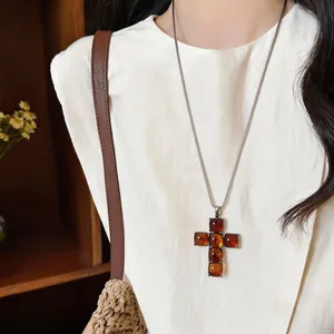 Detailed macro view of a vintage amber resin cross pendant necklace on a white linen shirt.