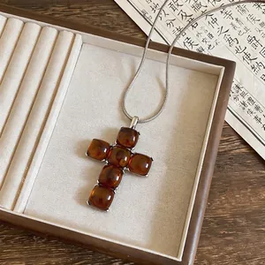 Close-up detail of amber resin cross pendant on a silver snake chain.