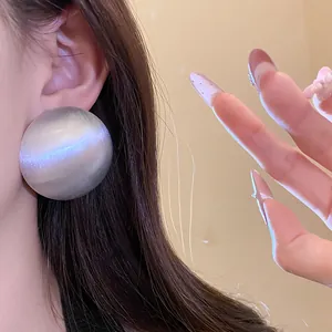 Detailed view of oversized round silver stud earrings with iridescent finish on model's ear