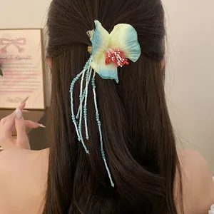 Detail of a tropical fabric flower hair clip with long bead tassels on dark brown hair