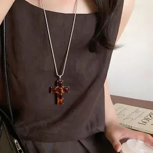 Close-up of a large brown resin cross pendant on a long silver-tone necklace chain