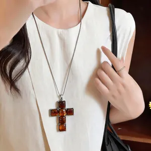 Close-up detail of amber resin cross pendant necklace on a minimalist cream blouse