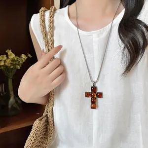Detail of a vintage resin cross pendant necklace worn by a model in a white linen shirt.