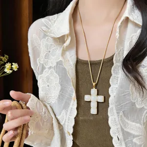 Close-up detail of a minimalist resin cross pendant necklace with gold chain worn on lace.