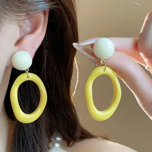 Close-up of yellow dopamine acrylic oval drop earrings with white spherical studs