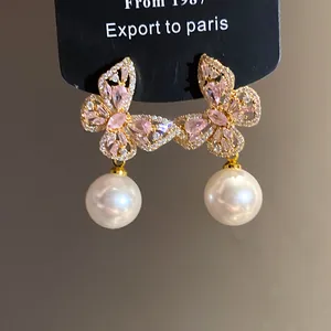 Gros plan de boucles d'oreilles papillon avec cristaux roses et perles blanches.