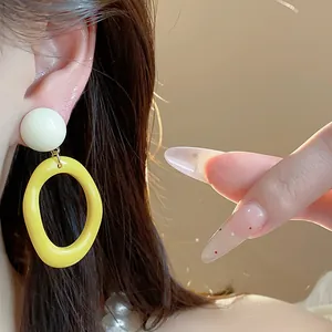 Close-up of yellow and white acrylic geometric hoop earrings worn on a model's ear.