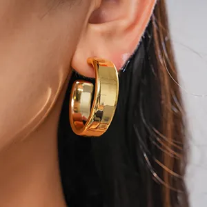 Close-up detail of a glossy gold C-shaped geometric hoop earring worn on a model's ear