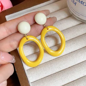 Detail of yellow acrylic oval drop earrings with cream round studs