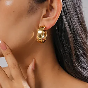 Detailed side view of chunky gold-tone C-shaped geometric hoop earrings on female model