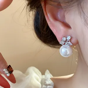 Close-up of elegant zircon pearl stud earring on model's ear with sparkly leaf design detail.