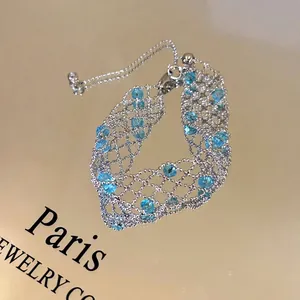Close-up of silver-tone lace bracelet with sparkling blue beads on golden surface.