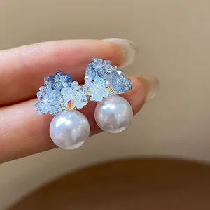 Close-up of elegant light blue zircon and white pearl stud earrings on silver needles