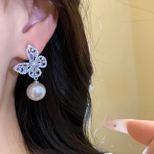Gros plan de boucles d'oreilles papillon en argent avec perle blanche sur l'oreille.