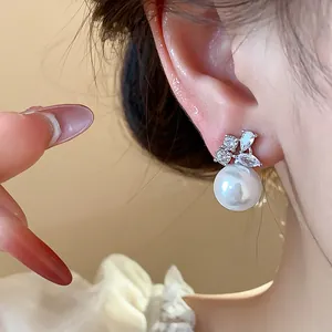 Detailed close-up of a silver needle earring with a large pearl and sparkling zircons.