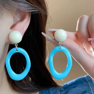 Detail shot of vibrant blue and white acrylic geometric drop earrings worn by a model.