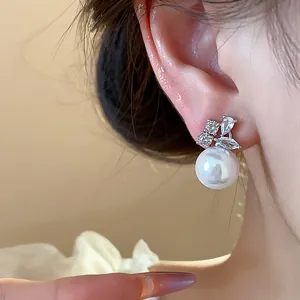 Close-up of elegant pearl stud earrings with sparkling zircon leaf accents on ear.