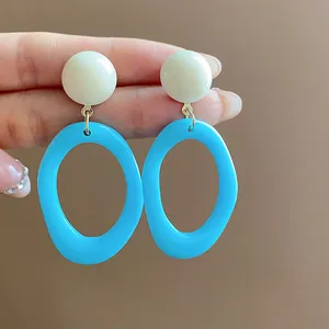 Close-up detail of blue acrylic oval hoop earrings with white round studs held by hand