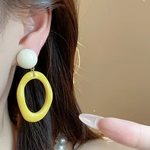 Close-up detail of stylish yellow and white acrylic geometric drop earrings worn by a model