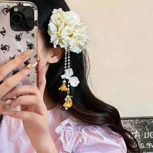 Detailed view of elegant white fabric flower hair clip with pearl tassels on wavy hair