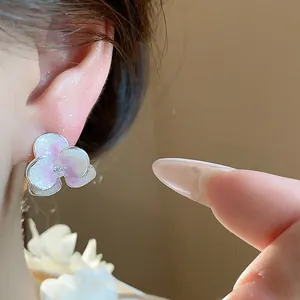 Close-up view of a delicate pearlescent flower stud earring featuring a small zircon center