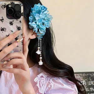 Detailed view of an elegant blue fabric flower hair clip with pearl tassels on a model