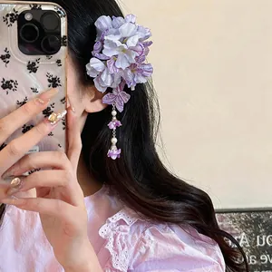 Detailed view of an elegant purple fabric flower hair clip with pearl tassels on a model