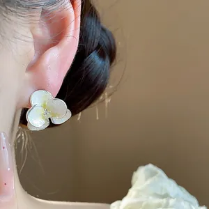 Close-up detail of a white enamel flower stud earring with zircon center on ear