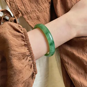 Close-up of elegant green chalcedony bangle on wrist with brown fabric background