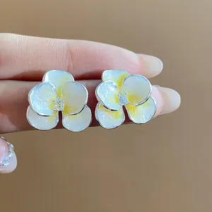 Detailed macro view of enamel flower stud earrings with shimmering yellow petals and zircon