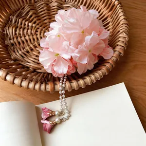Elegant pink fabric flower hair clip with pearl tassels displayed in a rustic basket scene.