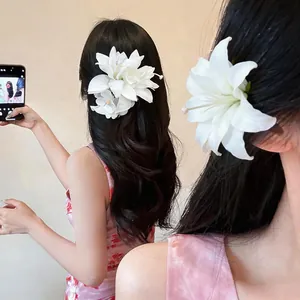 Detail of a white fabric lily flower hair clip worn by a model in a sweet vacation style.