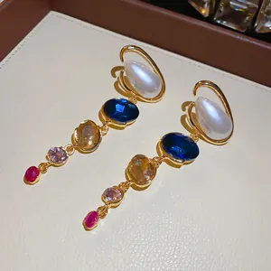 Macro view of multi-color gemstone drop earrings with teardrop pearls in gold setting.