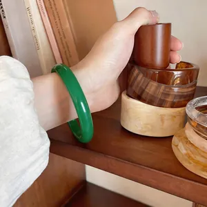 Close-up of a vibrant green chalcedony bangle on a wrist in a warm shelf setting