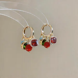 Dettaglio di orecchini a cerchio dorati stile vintage con ciondoli in pietre rosse e verdi