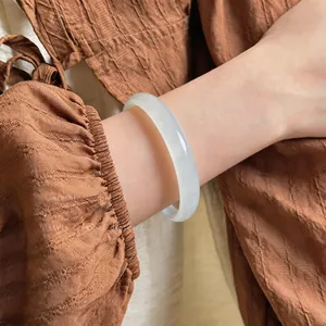 Close-up of elegant translucent white chalcedony bangle on wrist with brown fabric background