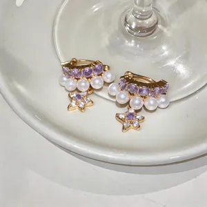 Dettaglio di eleganti orecchini a cerchio a stella con zirconi e perle bianche in oro.