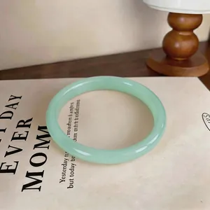 Elegant light green chalcedony bangle displayed on a minimalist book background.
