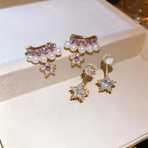 Dettaglio di eleganti orecchini a stella dorati con zirconi viola e perle bianche