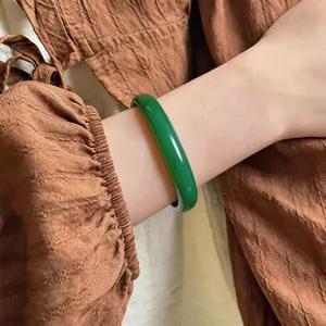 Close-up of elegant green chalcedony bangle worn on wrist with brown fabric background