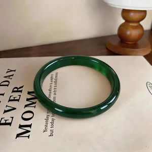 Detailed view of a translucent dark green chalcedony bangle on a book page with warm lighting.