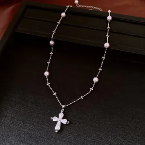 Primo piano di una collana d'argento con perle bianche e un ciondolo a croce di cristallo.