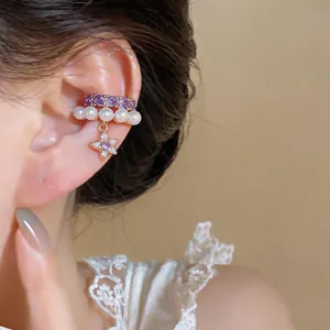 Dettaglio dell'orecchino a clip con stella, zirconi viola e perle indossato sull'orecchio.