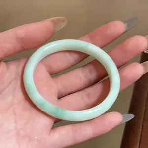 Detailed close-up view of a minimalist pale green chalcedony bangle bracelet held in hand