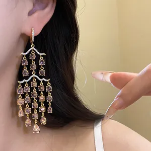 Detailaufnahme luxuriöser goldener Quastenohrringe mit rosa Zirkon und Wassertropfen