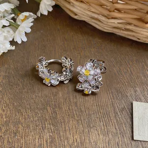 Close-up of elegant zircon flower earrings on rustic wood surface with white floral accents.