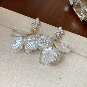 Macro detail of white petal shell earrings with sparkly zircon studs on a beige stand.