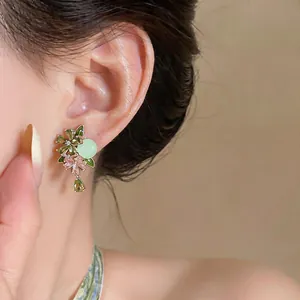 Close-up of elegant floral zircon stud earrings with green crystals on a female ear
