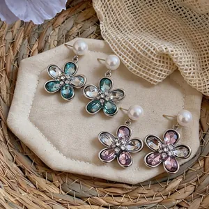 Elegant flower drop earrings with crystals and pearls on a straw mat background.